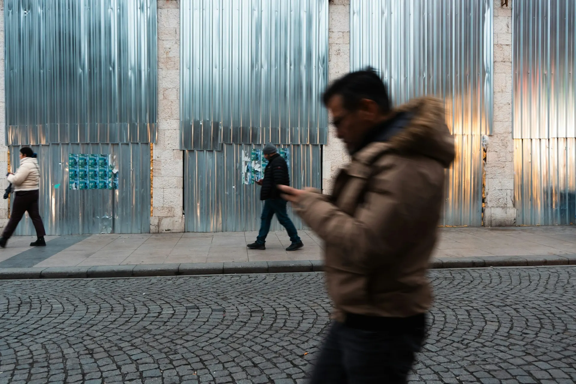 Ein Mann geht über eine gepflasterte Straße in der Stadt und schaut dabei auf sein Smartphone.